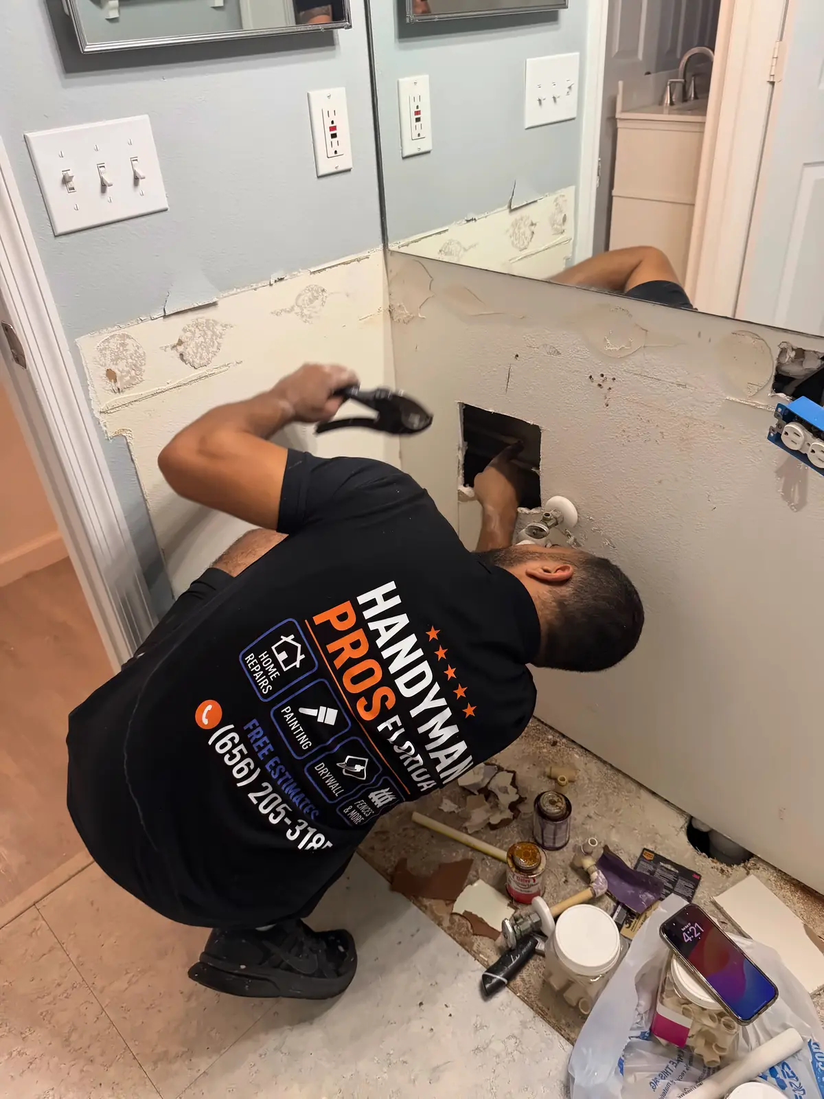 Handyman Pros Florida technician repairing bathroom plumbing through an opened drywall wall behind a removed vanity in a Tampa Bay home