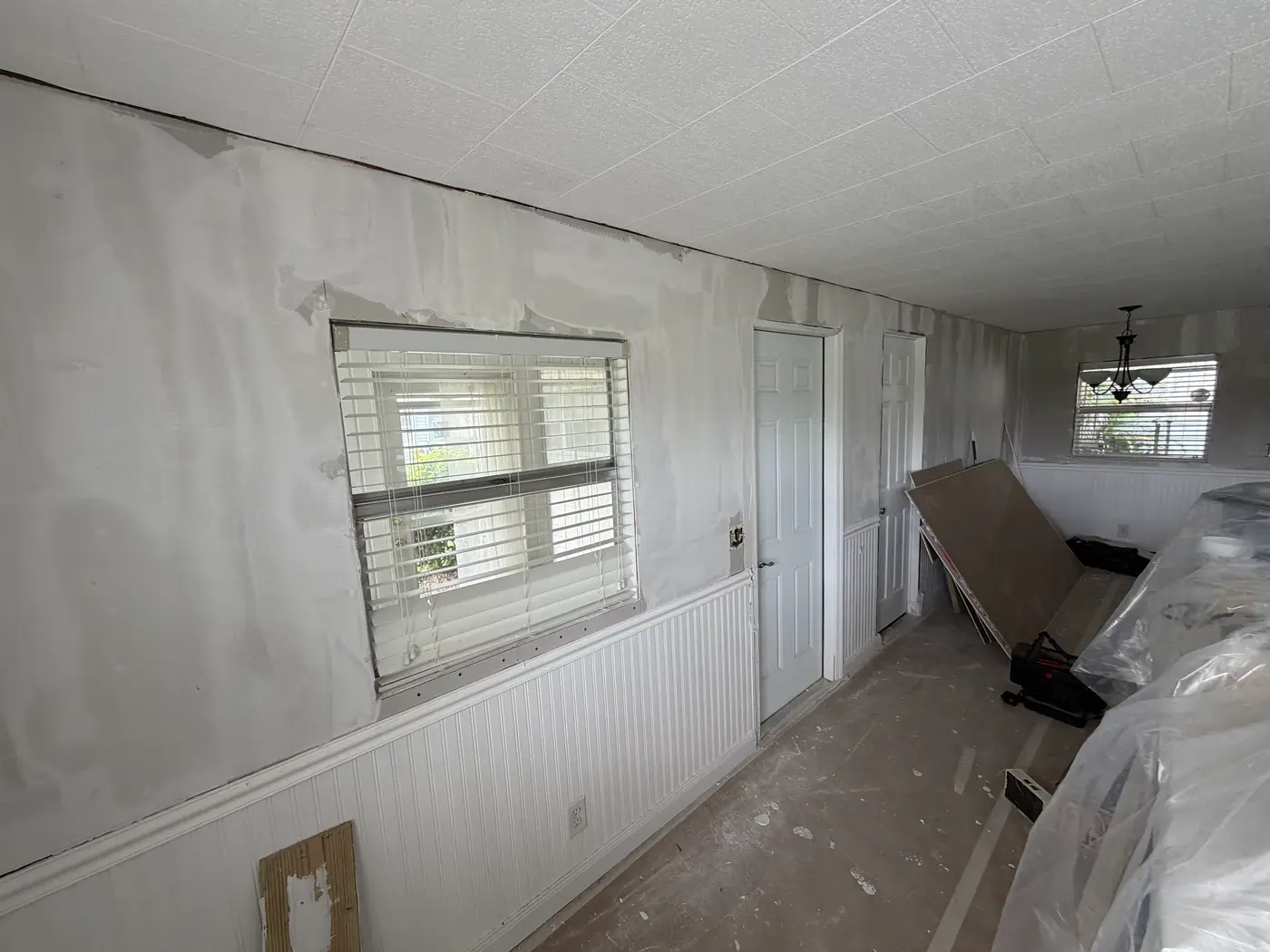 Unfinished room with drywall mud work around windows and a door, materials staged, Handyman Pros Florida